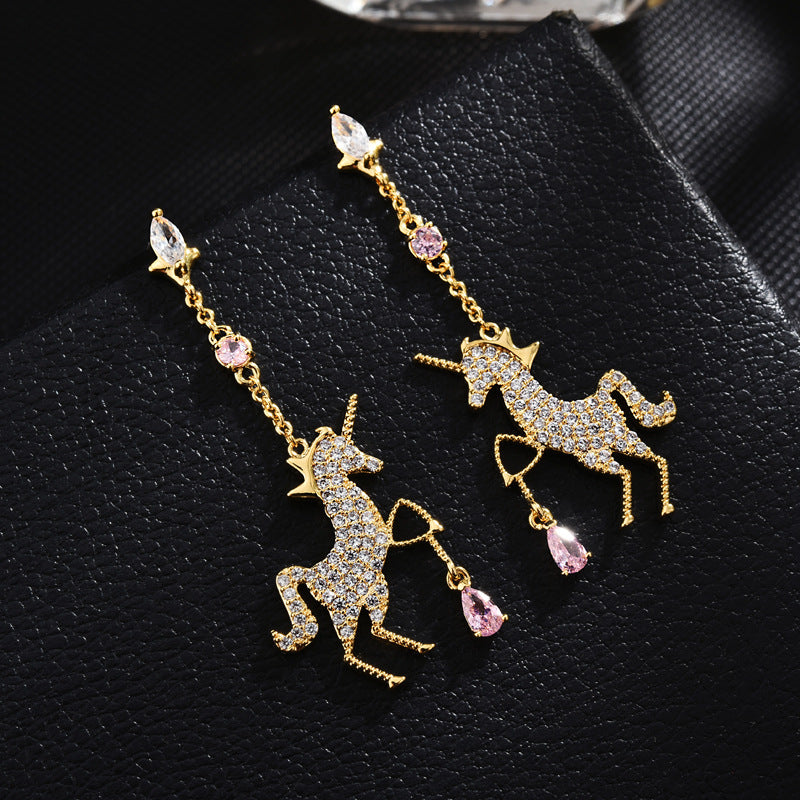 Unicorn-shaped earrings with gemstones on a black textured surface
