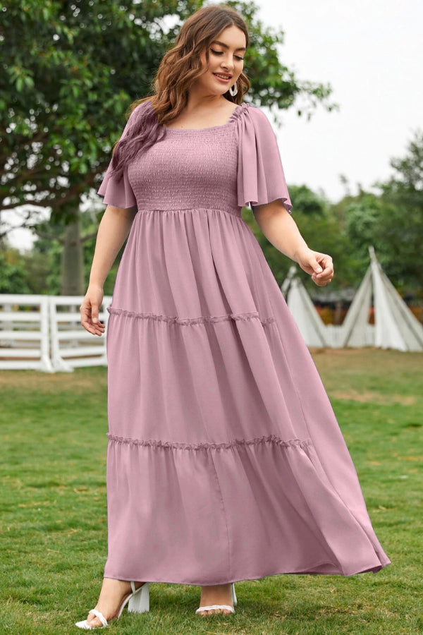 A woman wearing a green maxi dress with a smocked bodice and flutter sleeves, standing outdoors.