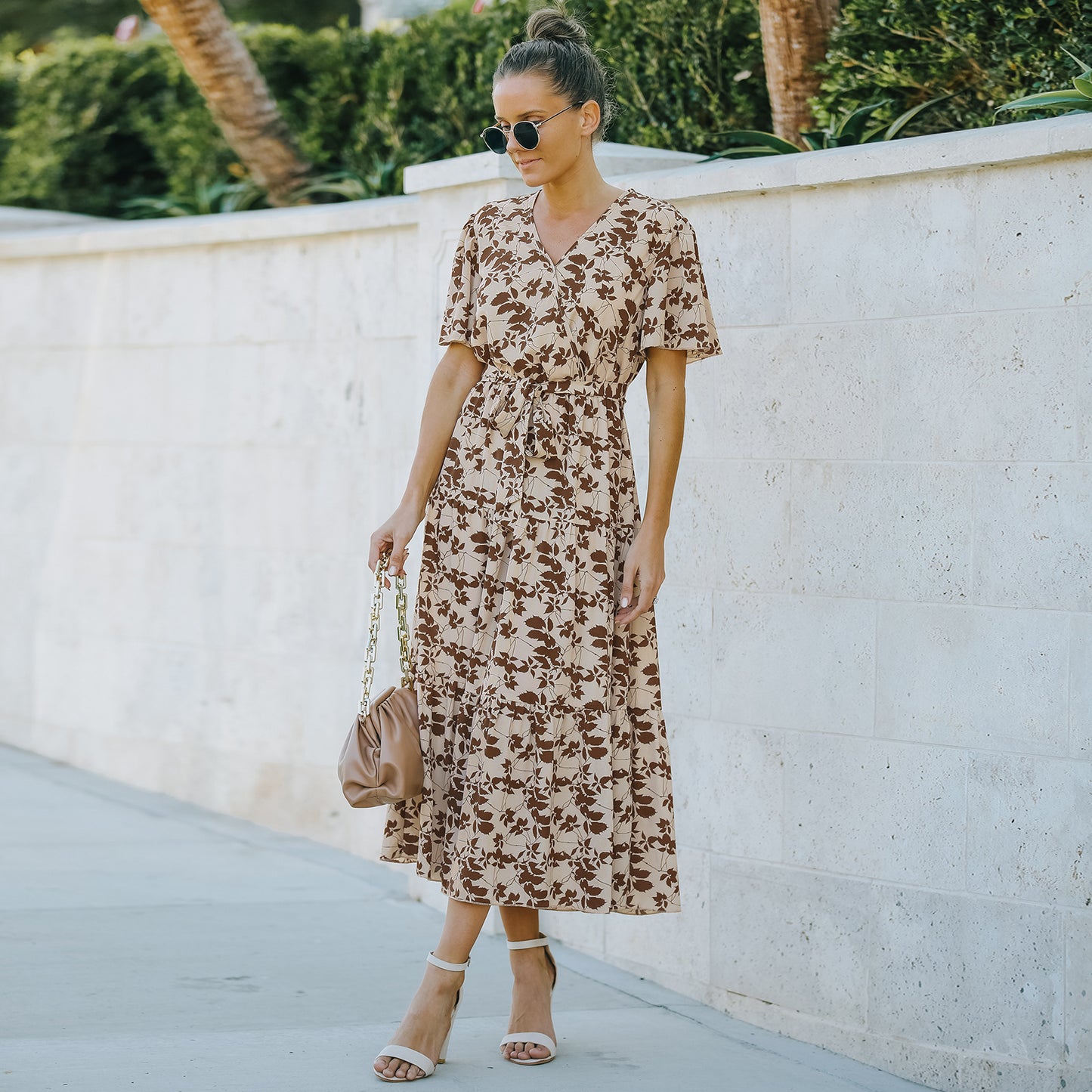 A woman wearing a floral midi dress with a V-neckline, short sleeves, and a belt at the waist. The dress is predominantly blue with a pattern of smaller white flowers.