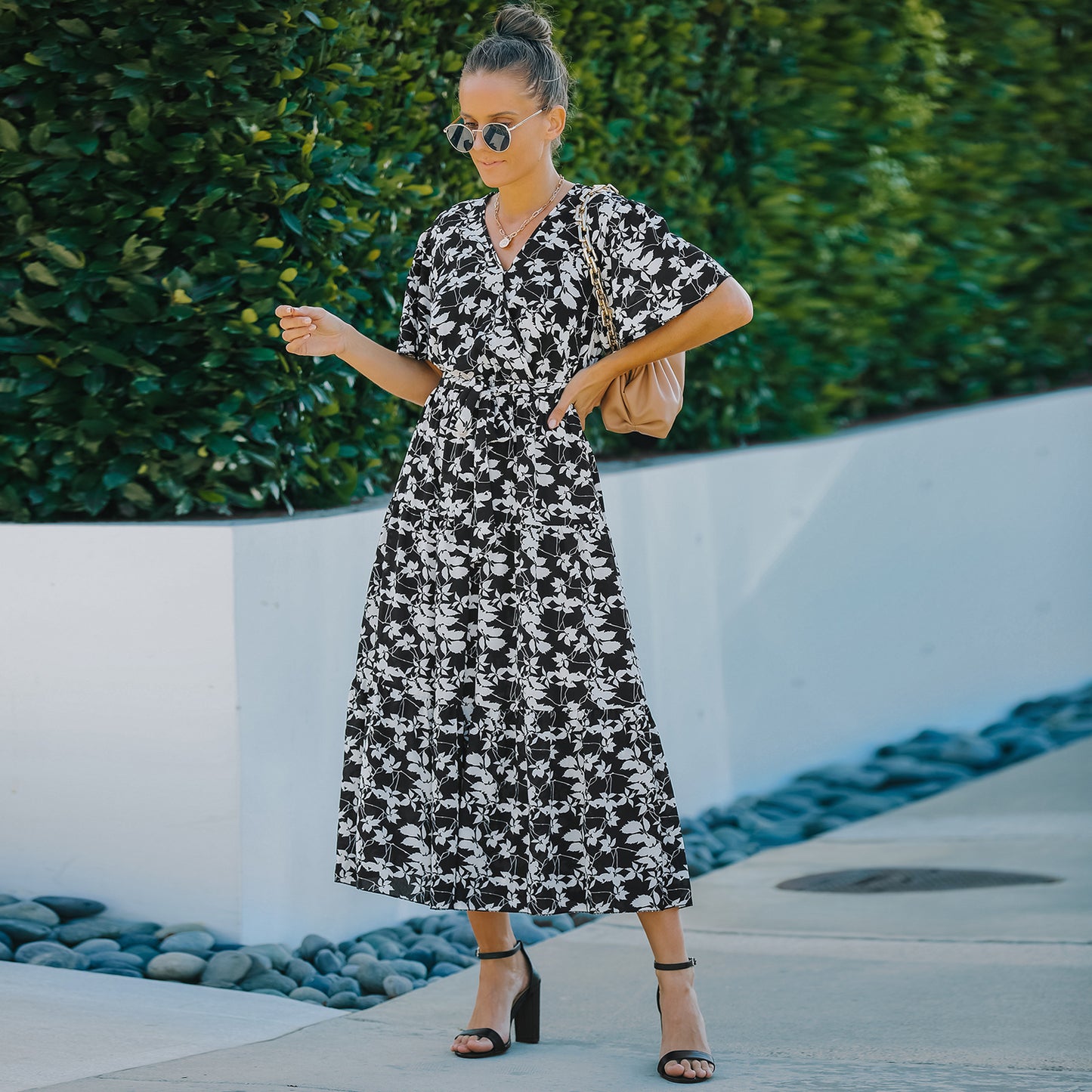 A woman wearing a floral midi dress with a V-neckline, short sleeves, and a belt at the waist. The dress is predominantly blue with a pattern of smaller white flowers.