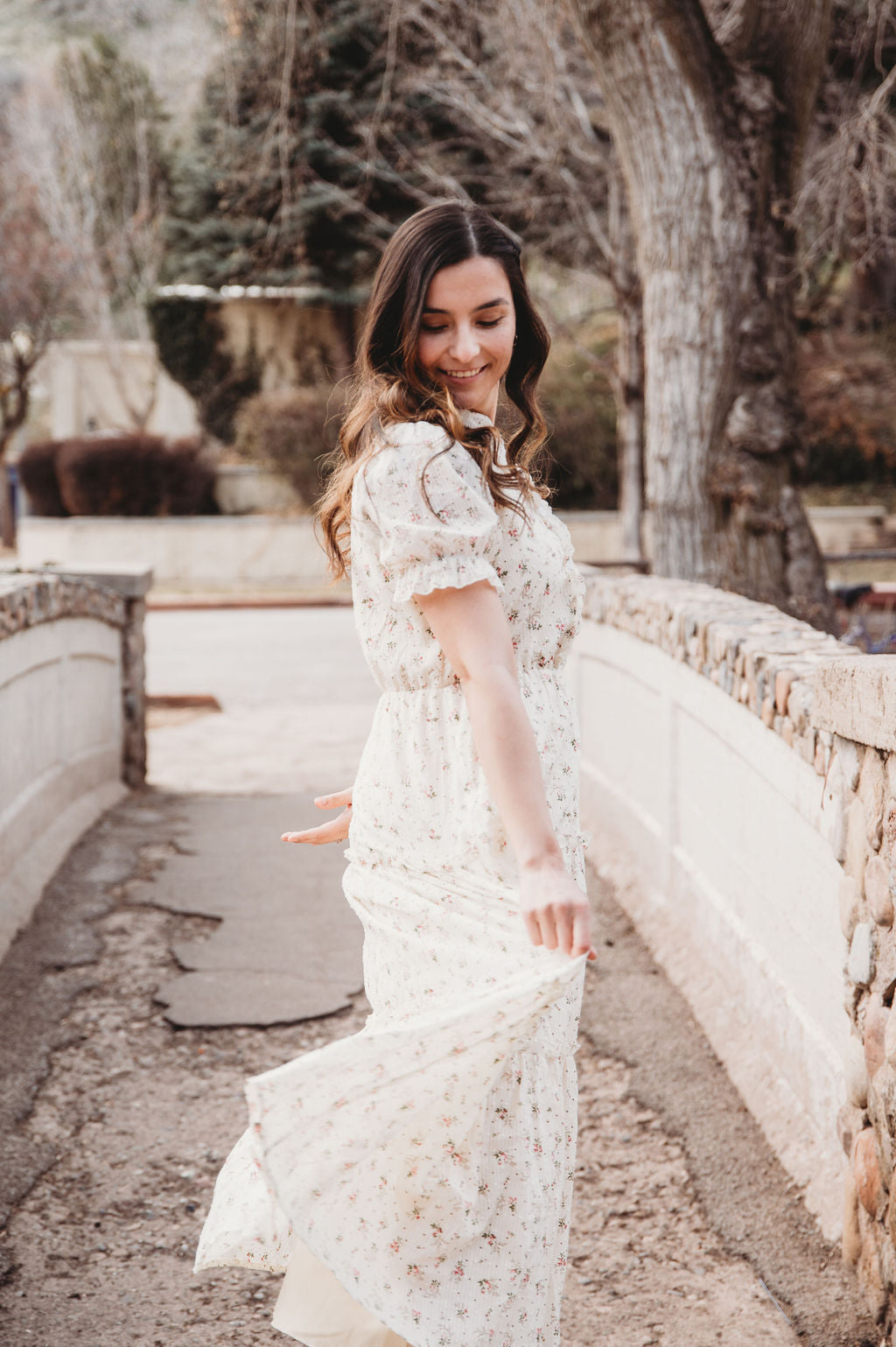Woman in a floral cotton dress twirling on a stone bridge, showcasing the elegance of the Floral Cotton Dress.