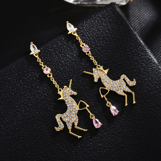 Unicorn-shaped earrings with gemstones on a black textured surface