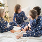 Four children in matching pajamas sitting on a bed with a Christmas tree in the background