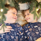 Two children wearing matching pajamas with a forest pattern, lying under a Christmas tree.