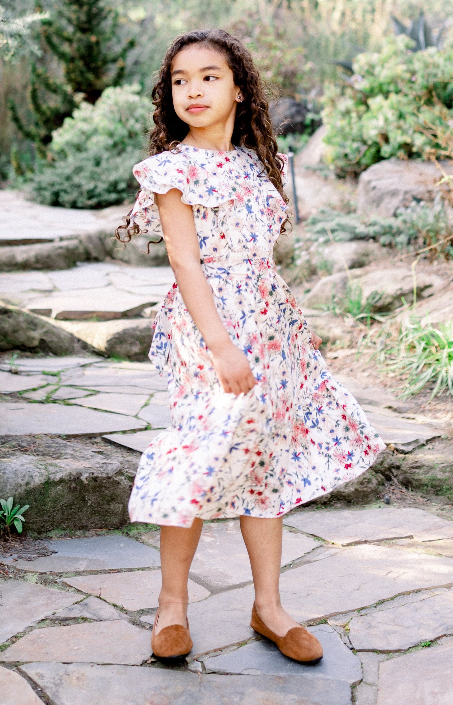 Young girl in a floral dress standing on stone steps in a garden