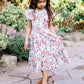 Young girl in a floral dress standing on a stone path with greenery in the background