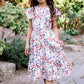 Young girl in a floral dress standing on a stone path in a garden.