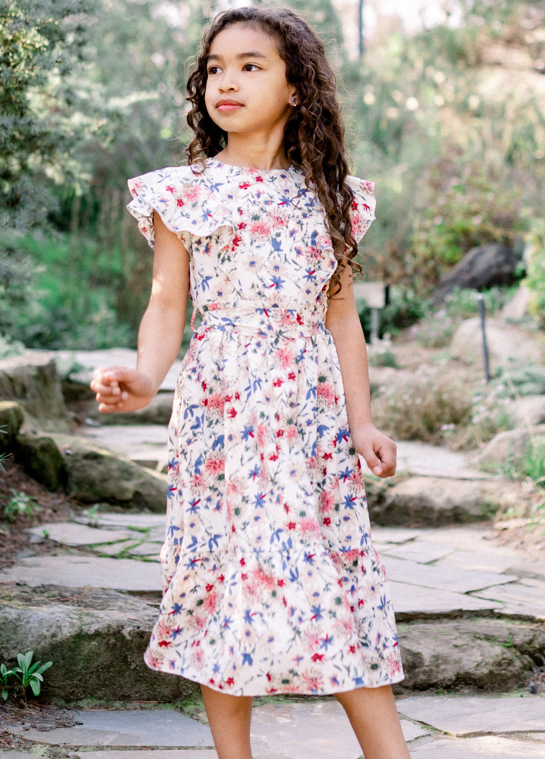 Woman in a floral dress standing on a stone path in a garden
