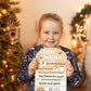 Child holding a personalized Christmas letter in front of a decorated Christmas tree.