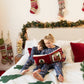 Two children reading a book on a bed decorated for Christmas.